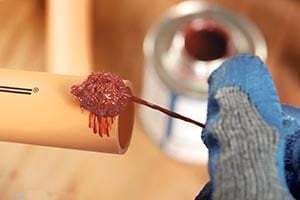 Person applying solvent cement to the end of an orange CPVC pipe while wearing gloves