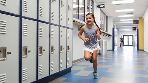 Girl running down the hallway next to lockers in a school
