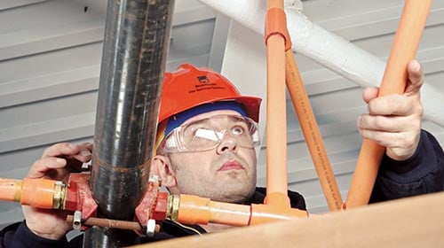 Man wearing red safety hat working with orange piping