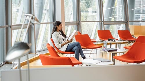 Woman sitting in orange chair looking a paper in a lobby setting