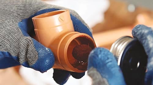 Person applying solvent cement to the end of piece of orange pipe