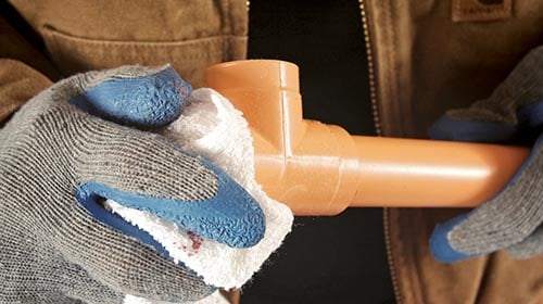 person wiping down a piece of orange pipe while wearing gloves