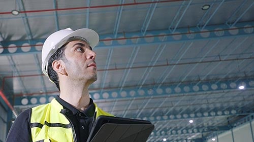 Man wearing white hard hat and safety vest looking off camera in a warehouse setting