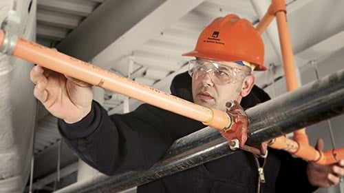 Man wearing orange safety hat and glasses looking to be installing orange pipes
