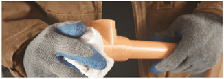 Person wearing gloves wiping down a piece of orange CPVC pipe