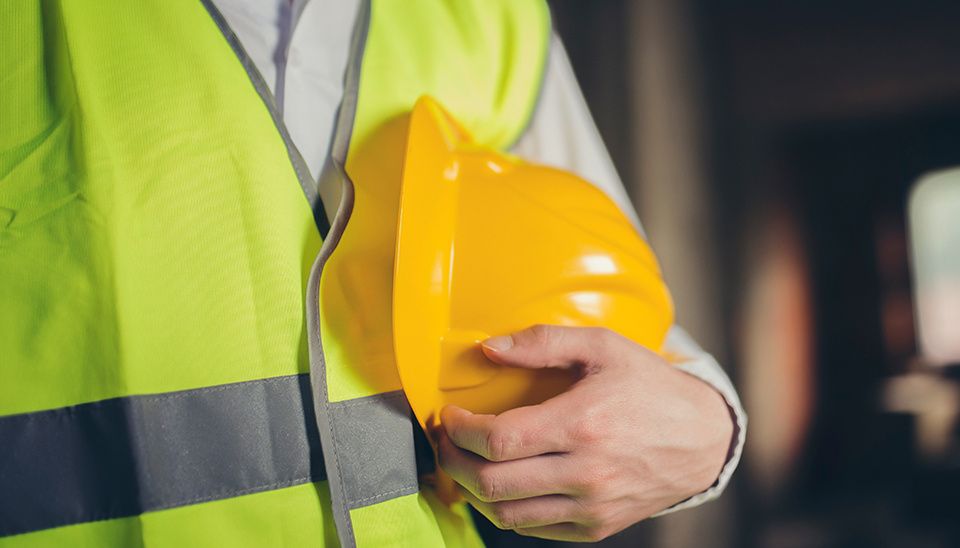 Person wearing reflective safety vest holding a yellow hard hat