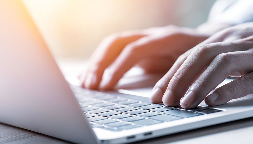 persons hands typing on laptop computer with light shining in the background