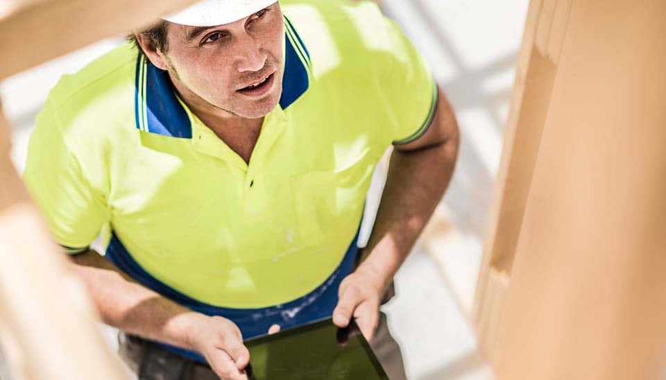 Man wearing bright yellow shirt and white hard hat on construction site looking up at equipment