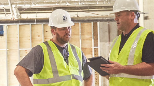 Two men in construction safety gear discussing items on an iPad