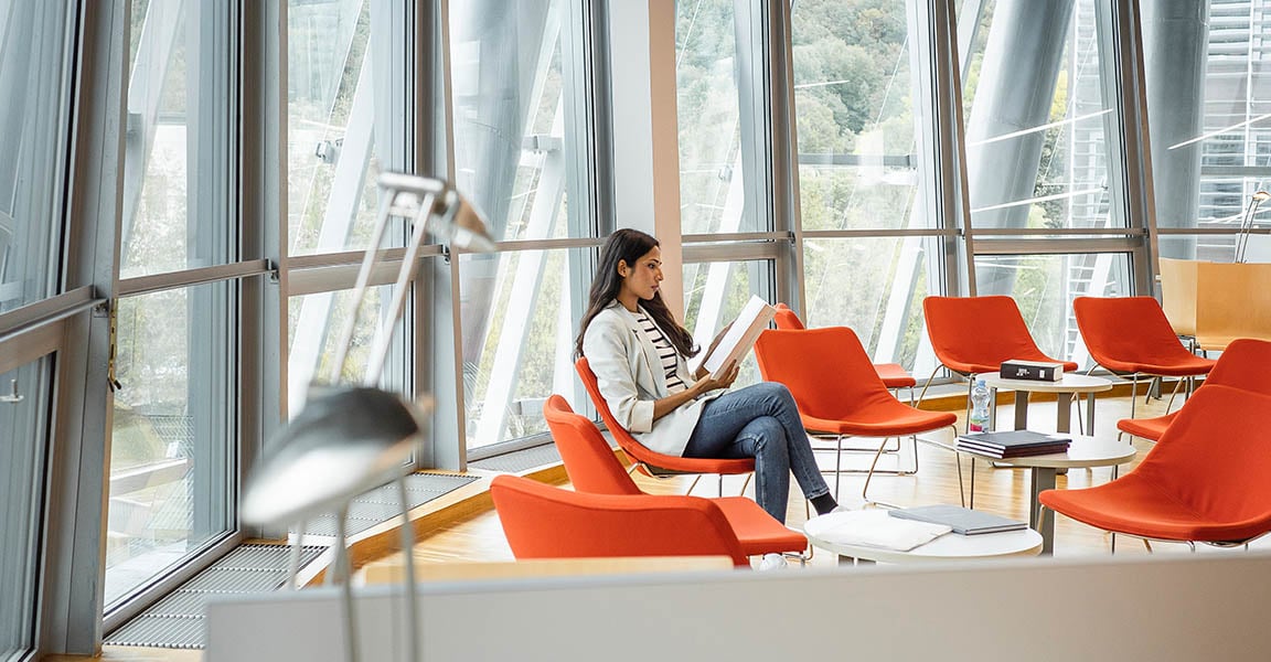 Woman sitting in what looks like an office setting lobby reading a book