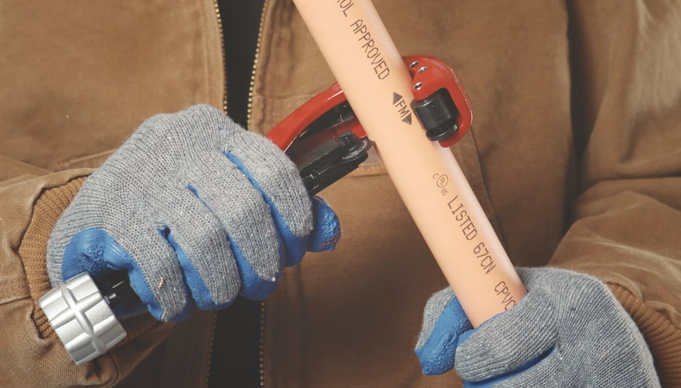 person wearing gloves cutting orange CPVC pipe